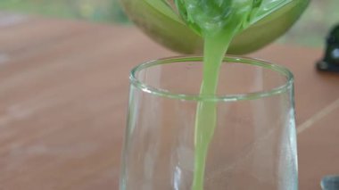 Yeşil meyve suyu bir bardağa dolduruluyor, ahşap bir masada buzla.