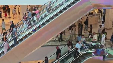 Müşteriler hareketli bir ticaret merkezinde yürüyen merdivenlere tırmanıp iniyorlar. Tiflis, Gürcistan - 8 Haziran 2025.