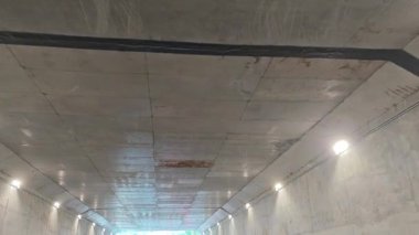 Tavanda ışıklar olan beton tünelde ilerliyoruz.. 