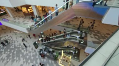 Bulanık müşteriler ve çalışanlar büyük, modern bir alışveriş merkezinde yürüyen merdivenlerde ilerliyorlar. Tiflis, Gürcistan - 8 Haziran 2025.