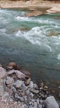 Kayalar ve bitki örtüsüyle çevrili bir nehirden temiz su akar.