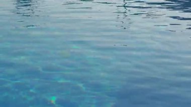 Turkuaz su yüzeyi, ışık yansımaları ve sakin bir yüzme havuzunda hafif dalgalanmalar.