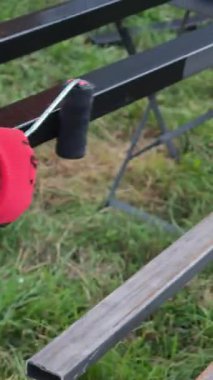 İnşaat işçisi uzun metal çubukları küçük silindirle siyaha boyayıp yaz günü açık hava bakım projesinde koruyucu kaplama uyguluyor.