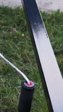 İnşaat işçisi metal yapıya küçük silindirli siyah koruyucu kaplama uyguluyor, bakım projesi sırasında çimenlik arazinin yakınında çalışıyor.