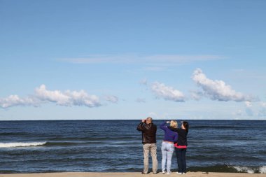 Dürbünlü bir grup insan Baltık Denizi kıyısına bakıyor.