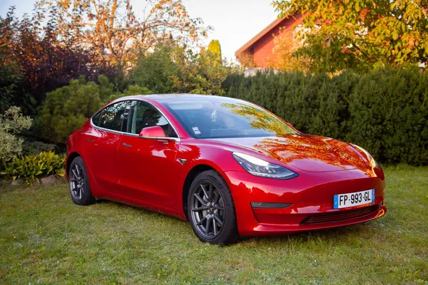 Vilnius, Litvanya - 15-08-2024 - Kırmızı Tesla Model 3 çift motorlu ev yakınındaki çimenlikte