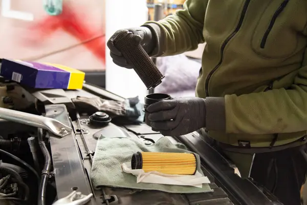 Auto mechanic is replacing an old oil filter on the new one in a car
