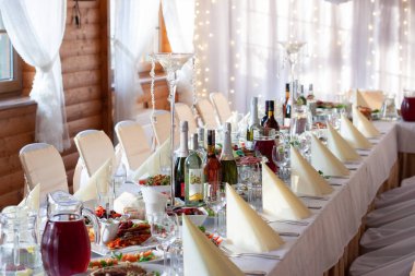 Bayram için dekore edilmiş bir ziyafet salonunda şarap şişeleri, bardaklar, tabaklar ve diğer yemeklerle süslenmiş bir ziyafet masası.