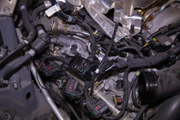 Motor kapağı çıkarılmış, bujiler çıkarılmış ve kablolar açığa çıkmış bir arabanın kısmen parçalanmış motor bölmesi.