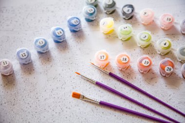 Resim için rakamlar, fırçalar, üzerinde numaralar olan küçük boya kapları ve önceden çizilmiş dış hatları olan bir tuval.