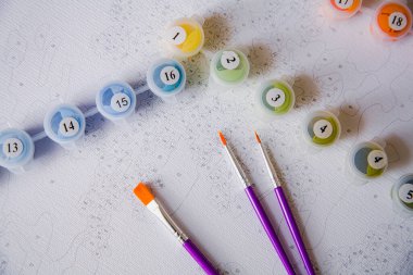 Resim için rakamlar, fırçalar, üzerinde numaralar olan küçük boya kapları ve önceden çizilmiş dış hatları olan bir tuval.