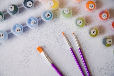 Resim için rakamlar, fırçalar, üzerinde numaralar olan küçük boya kapları ve önceden çizilmiş dış hatları olan bir tuval.