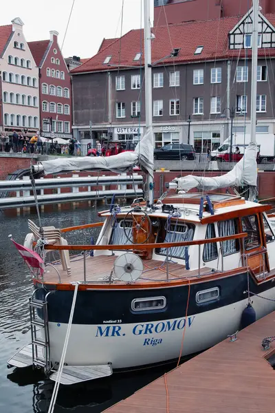 Gdansk, Polonya - 04-07-2025 - Ahşap güverteli, katlanır sandalyeli ve geleneksel liman kasabası cephelerinin önündeki deniz donanımlı şehir kanalında demirli bir yat