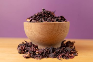 Dry hibiscus tea  in bowl on wooden board. violet background behind. herb. herbal tea. food ingredient.