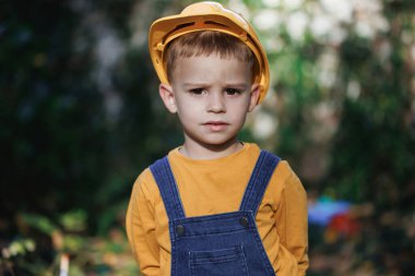 Little builder in helmet. Child dressed as a workman builder. Portrait little builder in hardhats. Caucasian industry worker smiling confident for camera while coworking on construction site.