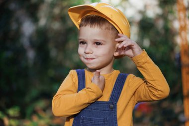 Caucasian industry worker smiling confident for camera while coworking on construction site. Little builder in helmet. Child dressed as a workman builder. Portrait little builder in hardhats.