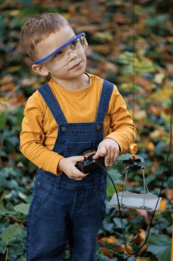 Little boy engineer builder architect in safety glases. Portrait of little boy with remote control from radio-controlled toy mobile construction crane in the park in the autumn.