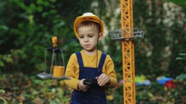 Little boy builder in uniform working on construction site. Child future engineer builder architect with safety helmets looking on cranes. Dreaming of future profession. Dream concept