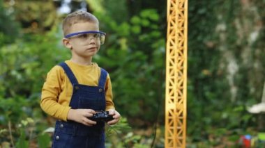 Portrait of little boy with remote control crane beam in an industrial warehouse. Little boy engineer builder worker is loading and unloading. Dreaming of future profession.