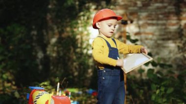 Little boy child future engineer builder architect with safety helmet with drawing, looking on new buildings and construction cranes on site. Future profession, big dream, building work concept, 4 K