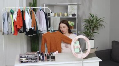 Boğazlı kazaklı moda blogcusu kadın akıllı telefon kamerasında sıradan renkli kazak gösteriyor. Moda kıyafetleri giyen stilist kadın kanalı için video bloğu bölümü çekiyor. Fikir lideri eğilimleri belirler.