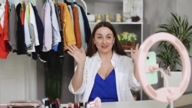 Kadın moda blogcusu akıllı telefon kamerasına kıyafetlerini gösteriyor. Kanal incelemesi için vlog bölümü çeken beyaz kadın stilisti..