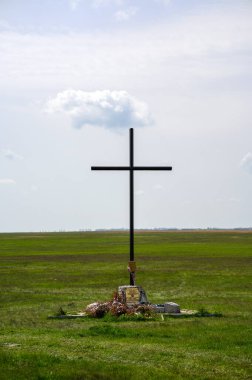 HORTOBAGY, HUNGARY 23 Nisan 2022 Koyu kahverengi bir ahşap haç çoğunlukla açık bir gökyüzünün altında tek bir kabarık beyaz bulut altında duruyor. Küçük renkli nesneler tabanın altına yerleştirilir