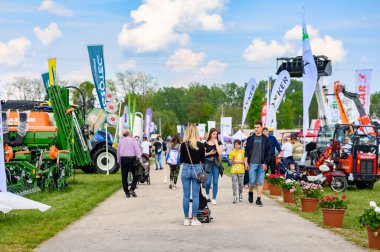 HODMEZOVASARHELY, HUNGARY MAYIS 06, 2022 Tarım fuarında güneşli bir gün, insanlar traktörler ve tarım makineleri, renkli bayraklar ve sancaklar arasında çakıl yolda yürüyor,