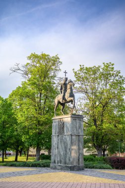 HODMEZOVASARHELY, HUNGARY MAYIS 06, 2022 Bronz bir binicilik heykeli, açık mavi gökyüzü altında yemyeşil ağaçlarla çevrili, bir taş kaide üzerinde dimdik duruyor. Heykel ana odak noktası, ayrıntılı.
