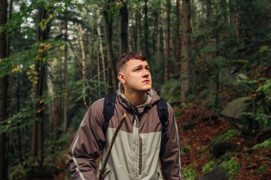 Ciddi bir genç adam yürüyüşçünün portresi ormanda bir yolda yürüyor ve ciddi bir yüzle başka yere bakıyor..