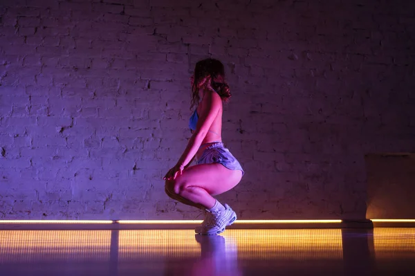 Attractive female twerk dancer dancing in dance studio in pink light on wall background.