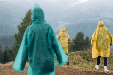 Dağlarda yağmurluk giymiş turistler bulutlu havada, dikiz manzaralı. Yürüyüş sırasında yağmurlu hava.