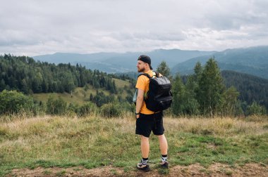 Sırt çantalı bir erkek turist güzel bir manzarayla bir dağın tepesinde duruyor ve başka yere bakıyor..