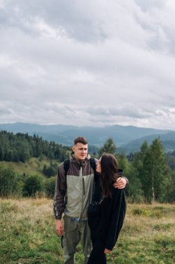 Genç ve güzel bir çift, erkek ve kadın, yürüyüş sırasında güzel manzaranın arka planında durup birbirlerini kucaklarlar. Dikey fotoğraf