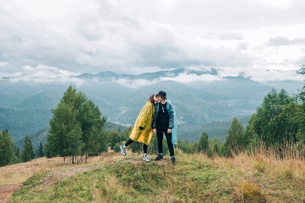 산에서 비옷을 구름낀 경치를 배경으로 동안껴안고 입맞춤을 귀여운 관광객 — 스톡 사진