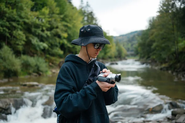 stock image Stylish guy tourist in panama and casual clothes is shooting a video in the mountains on an old digital camera.