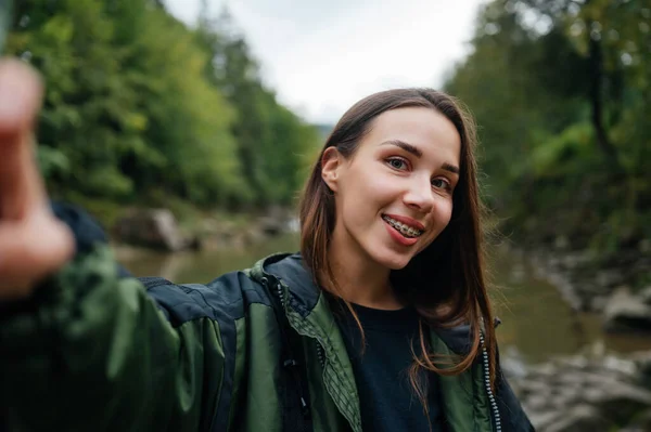 stock image Happy female tourist in the mountains taking a selfie with a smile on her face against the background of a fast mountain river