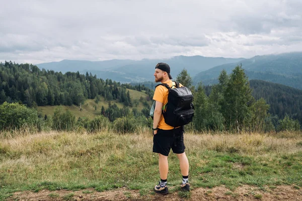 Samiec Turysty Luźnych Ubraniach Plecakiem Stoi Szczycie Góry Pięknym Krajobrazem — Zdjęcie stockowe