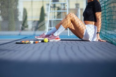 Tenis kortunda raket ve topun yanında oturan bayan tenisçinin yakın plan fotoğrafı. Tenis konsepti.