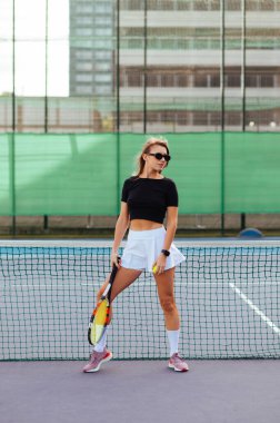 Çekici atletik bayan tenisçinin dikey portresi elinde raketle sahada kameraya poz veriyor..