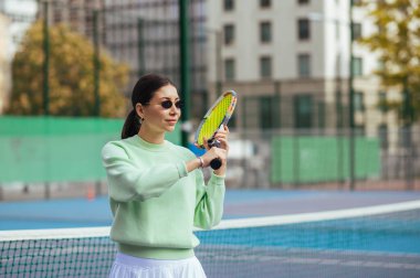 Antrenman sırasında sahada şık bir bayan tenisçinin portresi, yana bakıyor ve raketi sallıyor..