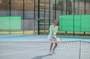 Elinde raketle kortta tenis oynayan ve ciddi bir yüzle yüzünü çeviren sportif bir kadının portresi. Tenis konsepti.