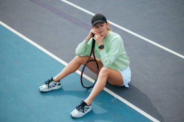 Şapkalı güzel bayan tenisçi sahada oturuyor ve zor bir maçtan sonra yüzünde gülümsemeyle dinleniyor.