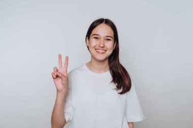 Genç Asyalı kadın gündüz vakti elini basit bir iç mekanda neşeyle barış işareti yapıyor.