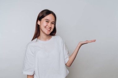 Asyalı genç bir kadın gülümsüyor ve avuç içi kadar kapalı bir alanda el kol hareketi yapıyor.