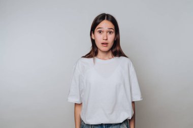 Tarafsız bir ifadeyle şaşırmış genç bir kadın gündelik kıyafetiyle arka planda duruyor.