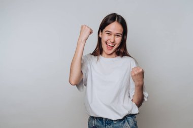 Genç Asyalı kadın başarıyı neşeli bir ifadeyle kutluyor. Tarafsız bir arka plana karşı günlük kıyafetle.