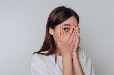 Genç bir kadın yüzünü tarafsız bir ortamda saklarken şaşkınlığını ve duygularını ifade eder.