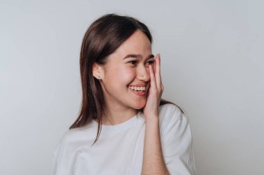 Gündüz vakti gülümseyen ve şakacı bir şekilde yüzünü kapalı bir alanda gizleyen genç bir kadın.