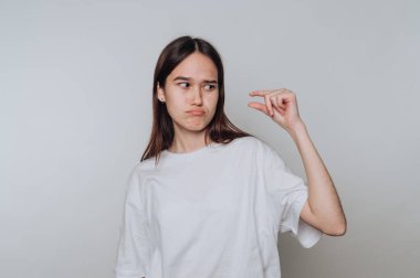 Genç Asyalı bir kadın basit bir arka planda küçük bir nesneden memnuniyetsizlik gösterirken neşeli bir jest gösteriyor.